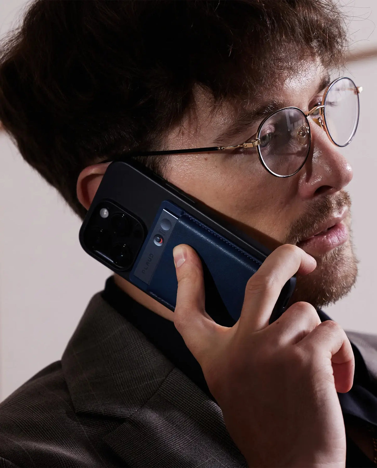 Uomo con occhiali parla al telefono, un Plaud Note blu scuro è attaccato al suo smartphone.